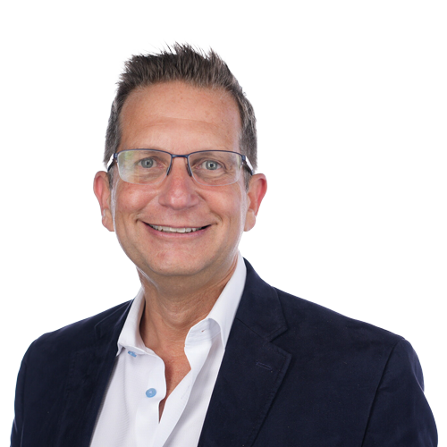 A middle-aged man with glasses, smiling, wearing a dark blazer over a white shirt against a plain white background.
