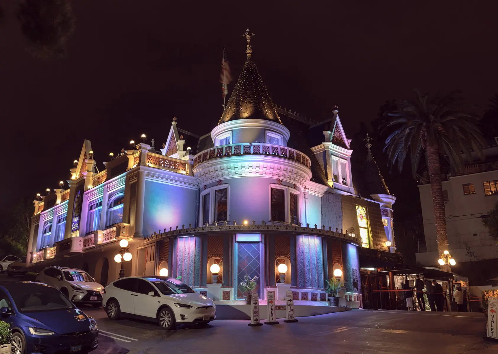 A whimsical building brightly illuminated at night, featuring vibrant colors, ornate architecture, and palm trees in the background.