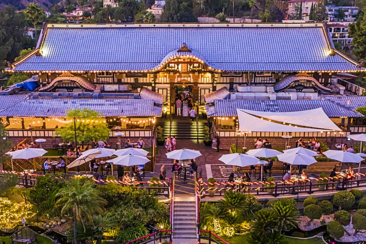 An elegant venue with a traditional Asian architectural style, surrounded by lush greenery and guests enjoying the outdoor dining experience at twilight.