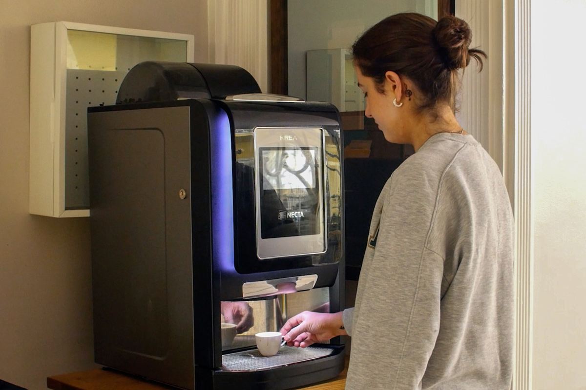 A person uses a modern coffee machine, pouring coffee into a small cup in a bright indoor setting.